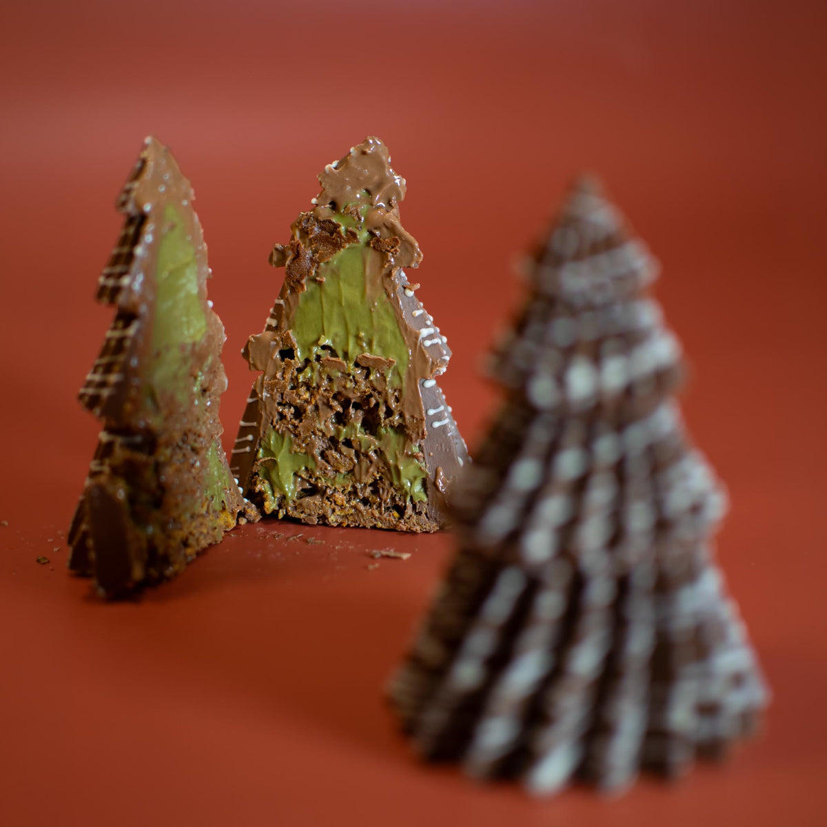 Two halves of a Little Christmas Tree showing the green pistachio filling, with a whole tree in front