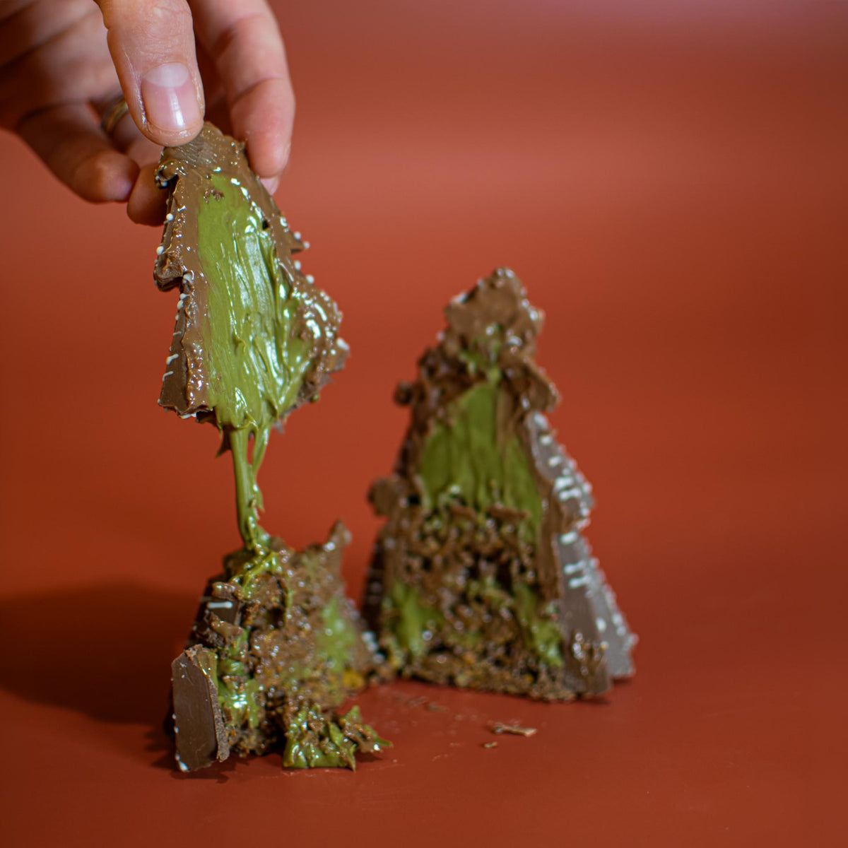 Hand pulling apart a Little Christmas Tree, with pistachio spread stretching between the two pieces