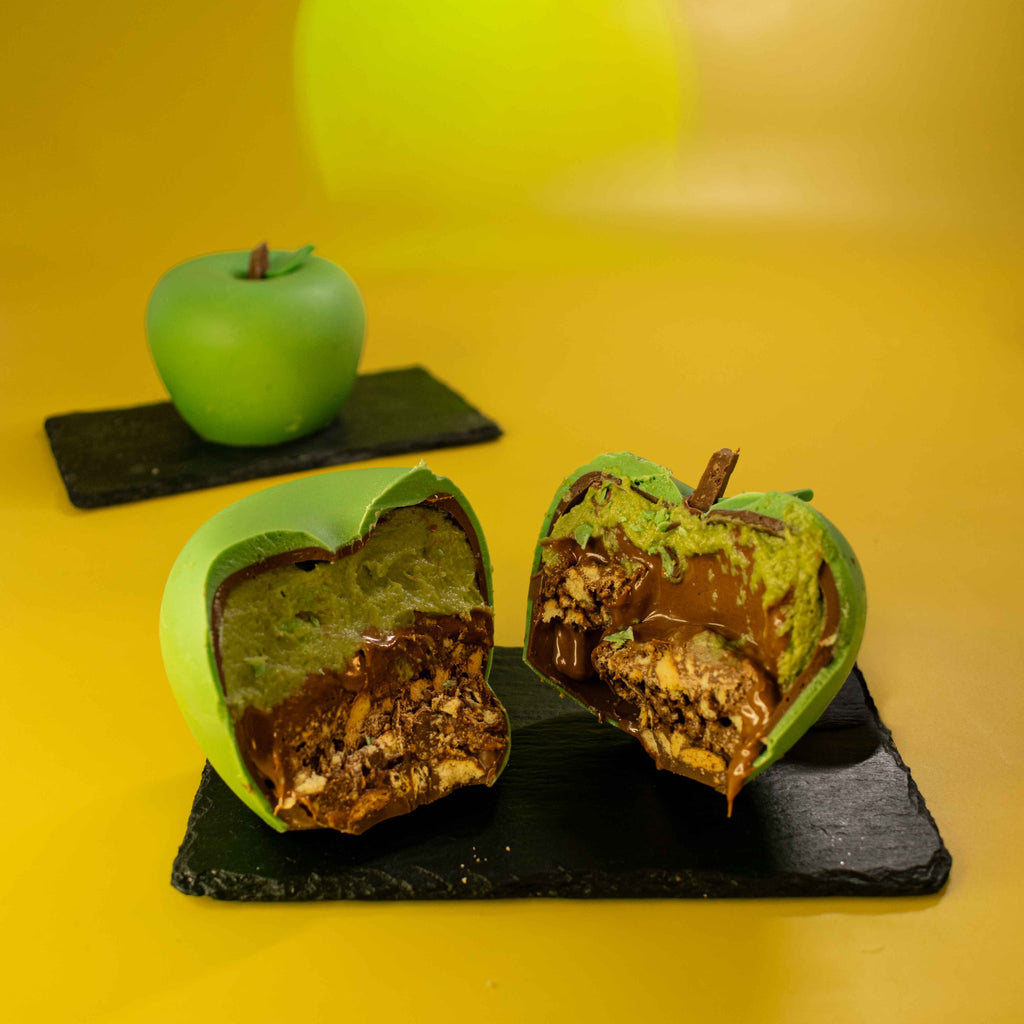 Chocolate apple cut in half showing green apple filling, hazelnut praline and chocolate crumble layers