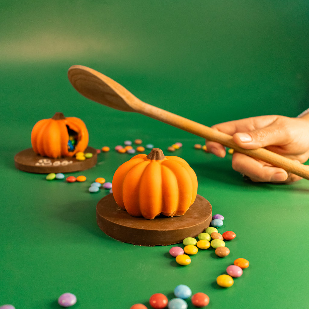 Wooden spoon about to smash a mini chocolate pumpkin