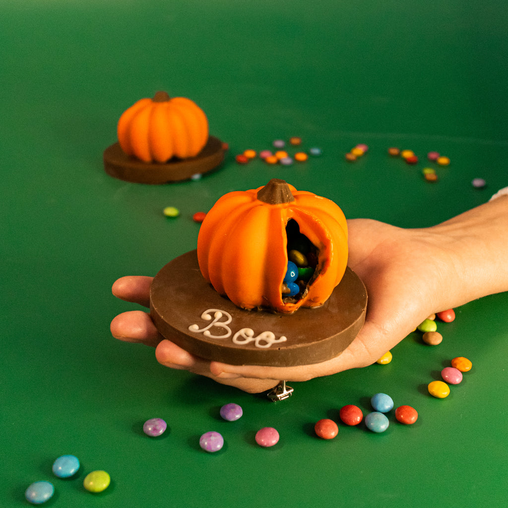 Hand holding a broken mini pumpkin with Smarties on a Boo plaque
