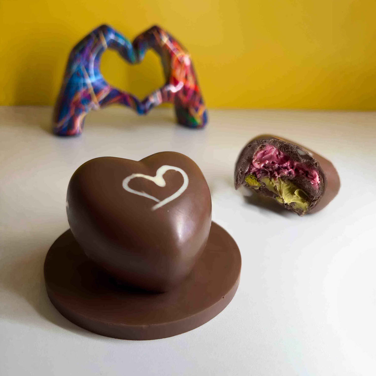 Roses & Pistachio milk chocolate heart on a plaque, beside a cut heart showing the pink rose and green pistachio filling